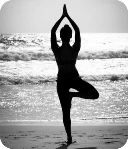 Silhouette of a person practicing a tree pose yoga stance on a beach at sunset